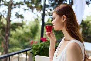 joven elegante mujer en un blanco vestir bebidas café al aire libre en un café verano día foto