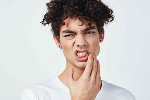 guy in white t-shirt with curly hair pain in the teeth health problems photo