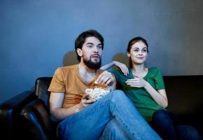 a man and a frightened woman watching a movie in the evening on the couch with a plate of popcor photo