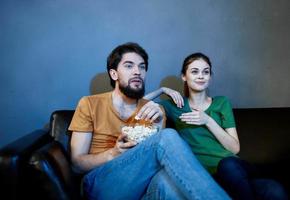 un hombre y un asustado mujer acecho un película en el noche en el sofá con un plato de palomitas de maíz foto