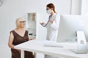 mayor mujer vistiendo un médico máscara en examen por un enfermero estetoscopio foto