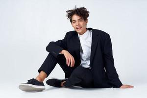 elegante joven hombre en traje se sienta en el piso y zapatillas Rizado pelo Moda foto