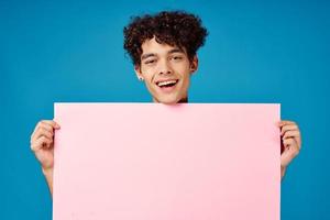 man with curly hair holding pink poster banner blue background photo