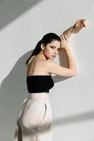 stylish woman in white pants and a short T-shirt leaned against the wall and a bright light photo