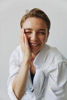 Young woman teenager listening to music with infertile headphones and dancing home, grinning with teeth with a short haircut in a white shirt on a white background. Girl natural poses with no filters photo