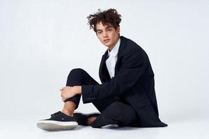 stylish young man in suit sits on the floor and sneakers curly hair fashion photo