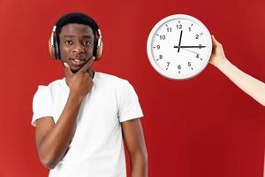 hombre de africano apariencia en auriculares siguiente a reloj en blanco camiseta recortado ver foto