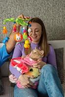 A young couple on the bed hugs their cat wrapped in a baby blanket and plays with her with a baby rattle. Conscious refusal of a couple to have children, treatment of pets as children. photo