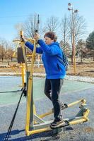 A retired woman with a backpack on her shoulders on an active walk outdoors is engaged in exercise equipment in the park. Senior woman taking care of her health photo