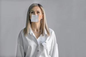 un rubia mujer, un blanco sábana de papel para texto es pegado en su boca. el prohibición en el expresión de sentimientos y emociones foto