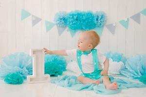 A beautiful one year old boy in turquoise clothing reaches for t photo