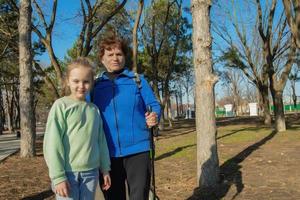 An elderly athletic woman walks in the park on a sunny day with her granddaughter. Care and care in the family for the older generation. photo