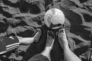 piernas mamá, padre y hijo en el playa en el arena siguiente a un fútbol pelota foto