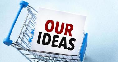 Shopping cart and text our ideas on white paper note list. Shopping list concept on blue background. photo