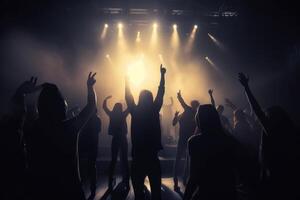 Black silhouette of a huge crowd of cheering people in front of a rock stage with soft bokeh lights created with technology. photo