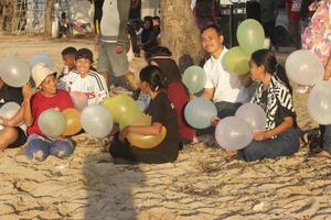 Atambua, Nusa Tenggara Timur, 2022 Tourists sitting on the white sand beach under a tree holding several colorful balloons are exposed to the sun photo