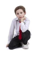 el niño se sienta en un blanco antecedentes. elegante chico en un blanco camisa aislado. Siete año antiguo niño en un atar. primario colegio alumno. foto
