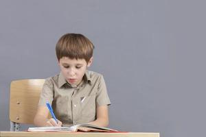 The child at the table is doing homework. Primary school student with a textbook. photo