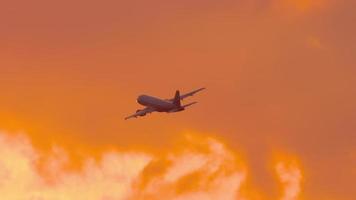 Airplane silhouette flies in the sunset fiery sky, gaining altitude. Cinematic shot of an airplane flying away. Tourism and travel concept video