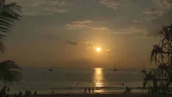 espaço de tempo, encontro uma dourado pôr do sol em a oceano costa. silhuetas do pessoas em a fundo do a pôr do sol. iates dentro a mar video