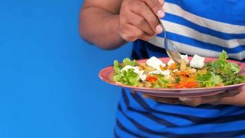 hungry guy eating salad in a plate, copy space blue background video