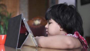 criança menina usando digital tábua sentado em uma mesa video