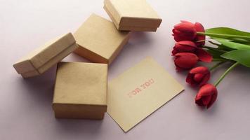Top view of gift box, envelope and tulip flower on color background video