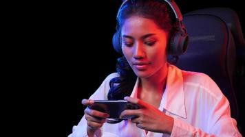 Esport Spieler Frau spielen Spiel online auf Smartphone beim heim. asiatisch Frau steuern Konsole mit Clever Telefon im Video Spiel. jung Frau Freizeit Spiel im dunkel Zimmer und schwarz Hintergrund beim heim.