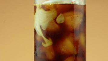 Coffee mixed with poured milk cream. Cream into black coffee and ice video