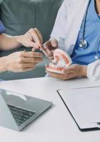 Male dentist with plastic jaw model on light background photo