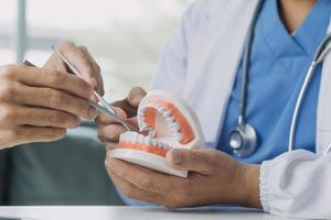 Male dentist with plastic jaw model on light background photo