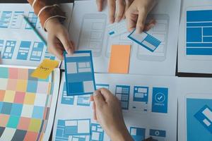 Close up ux developer and ui designer brainstorming about mobile app interface wireframe design on table with customer breif and color code at modern office.Creative digital development agency photo