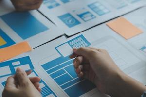 Close up ux developer and ui designer brainstorming about mobile app interface wireframe design on table with customer breif and color code at modern office.Creative digital development agency photo