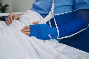 Man with broken arm in cast lying on bed in hospital. The emergency center treatment is plaster and hangs with sling for a further cure in an orthopedic clinic. Patient pain from accident injury. photo