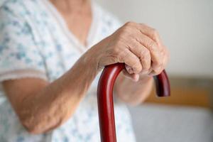 Asian elderly disability woman holding waling stick, wood cane, round handle, walking aid for help to walk. photo