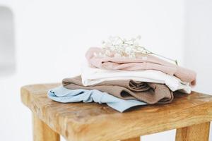 Stack of cotton tops in natural tones on wooden chair in bright room photo