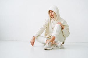 Young blonde woman in sportswear on background of white wall photo