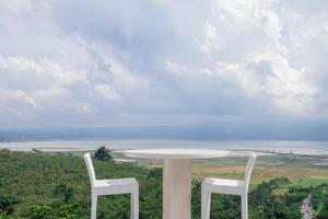 Empty white chair and table with beautiful background and cloudy sky. The photo is suitable to use for traditional food background, poster and food content media.