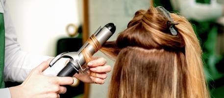 Hairdresser curling hair with curling iron photo