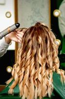 Hairdresser curling hair with curling iron photo