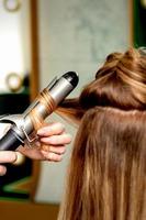 Hairdresser curling hair with curling iron photo