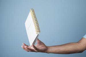 Blank notepad hovering over businessman's hand on light blue background, copy space for your text photo