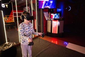 Boy kid playing game using virtual reality headset and gamepads in playing club. photo