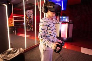 Boy kid playing game using virtual reality headset and gamepads in playing club. photo