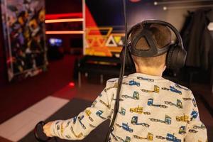 Boy kid playing game using virtual reality headset and gamepads in playing club. photo