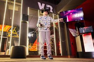 Boy kid playing game using virtual reality headset and gamepads in playing club. photo