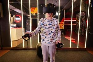 Boy kid playing game using virtual reality headset and gamepads in playing club. photo