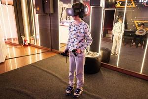 Boy kid playing game using virtual reality headset and gamepads in playing club. photo