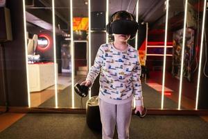 Boy kid playing game using virtual reality headset and gamepads in playing club. photo