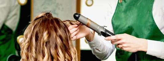 Hairdresser curling hair with curling iron photo